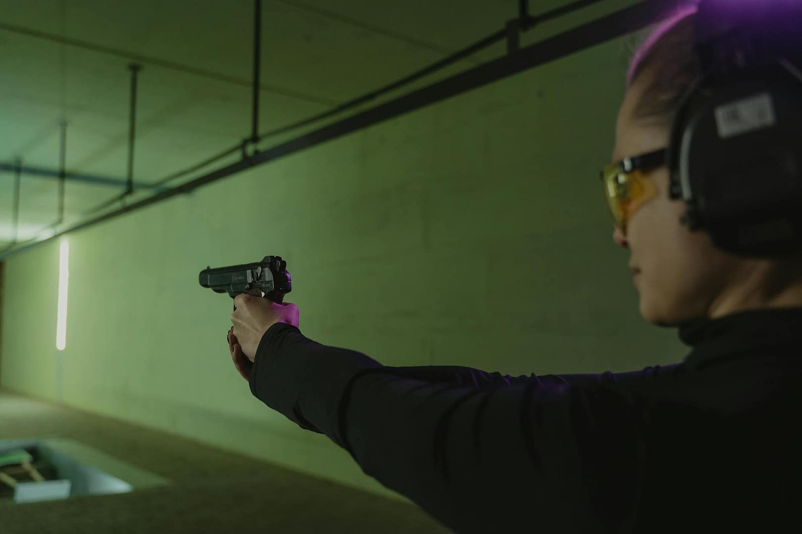 Focused woman at an indoor shooting range practicing target shooting with safety gear and a handgun.