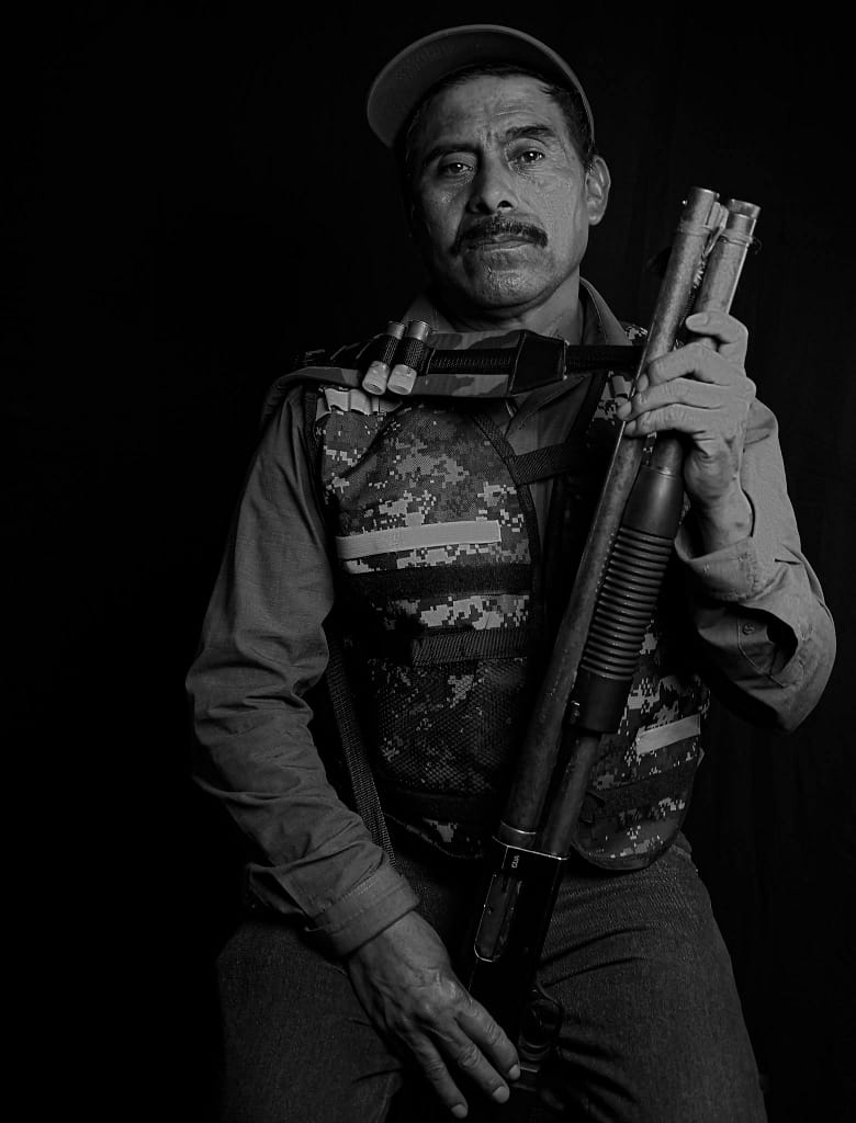 Black and white portrait of a soldier holding a shotgun, wearing a camouflage vest.