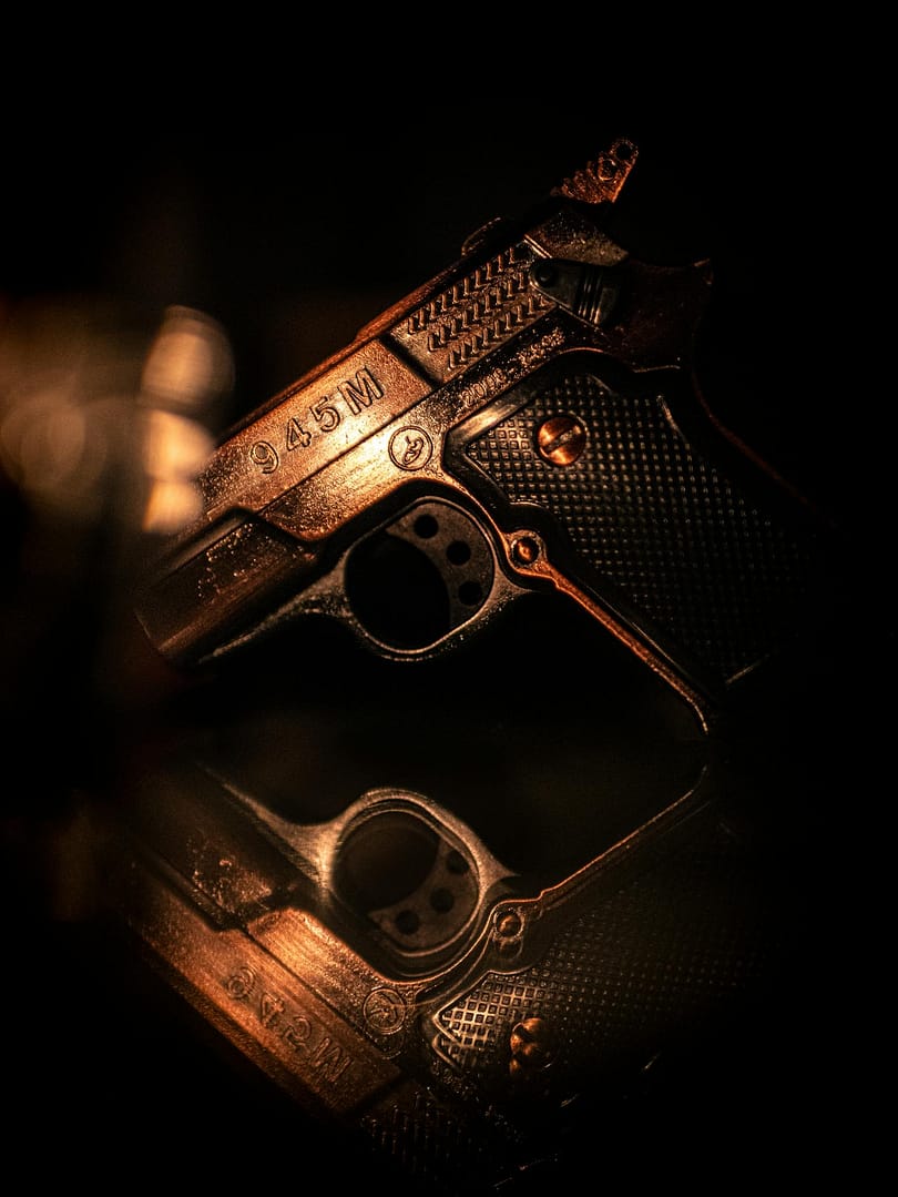 Close-up of a vintage handgun reflected on a surface in low light, artfully captured.